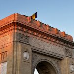 The Triumphal Arch in Bucharest, Romania, bathed in warm sunset light, showcases exquisite architecture.