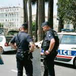 Police officers and a civilian interact near a police car on a busy city street.
