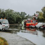 Emergency services attending a scene on a rainy road with rescue vehicles and personnel.