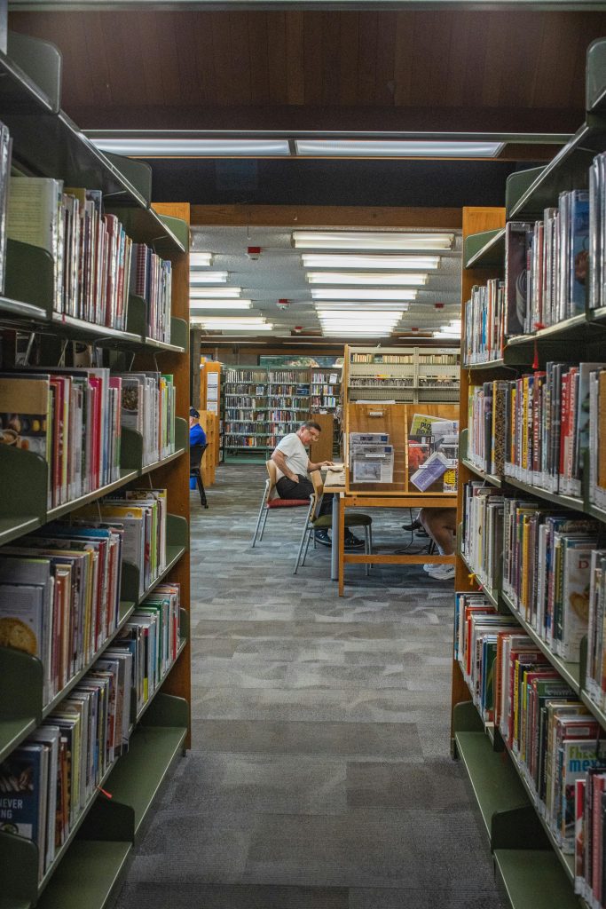 Adults studying in a cozy library aisle, surrounded by bookshelves. Ideal for education and reading concepts.