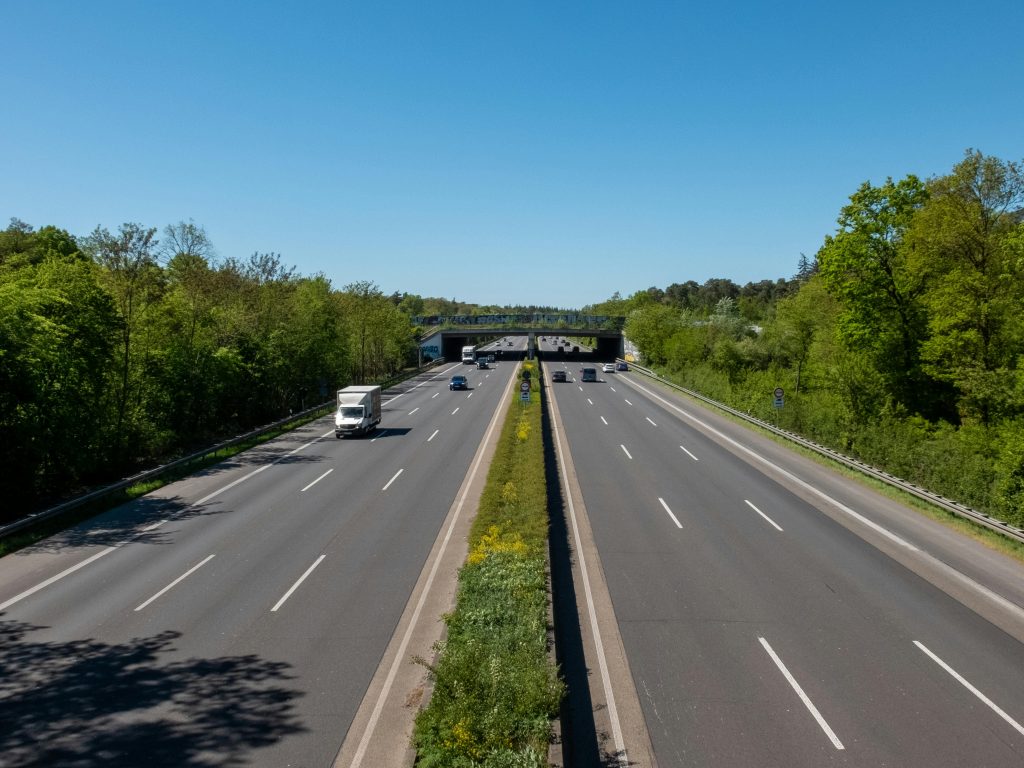 A clear highway under a bright blue sky with few vehicles, surrounded by lush greenery.