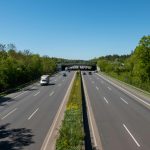 A clear highway under a bright blue sky with few vehicles, surrounded by lush greenery.