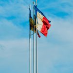 From below of waving flags of France Moldavia and Europe symbolizing unity of European countries placed against blue sky
