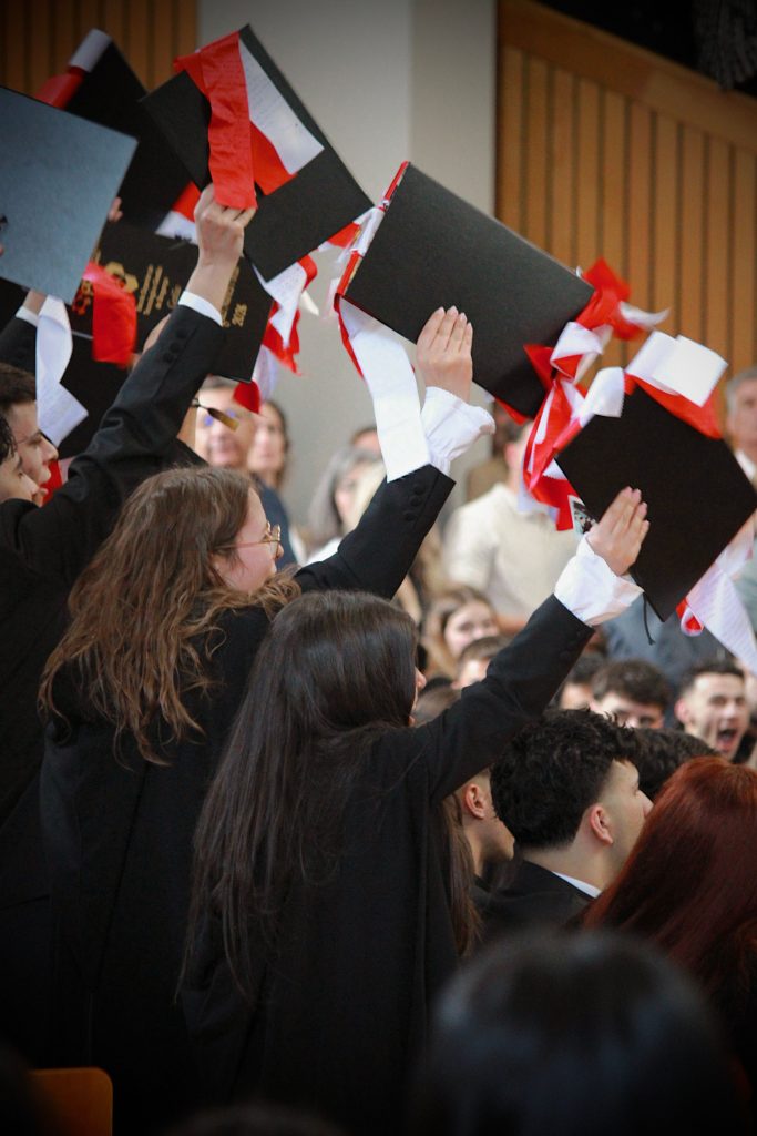 Students celebrate graduation by tossing caps indoors. Joyous academic milestone.